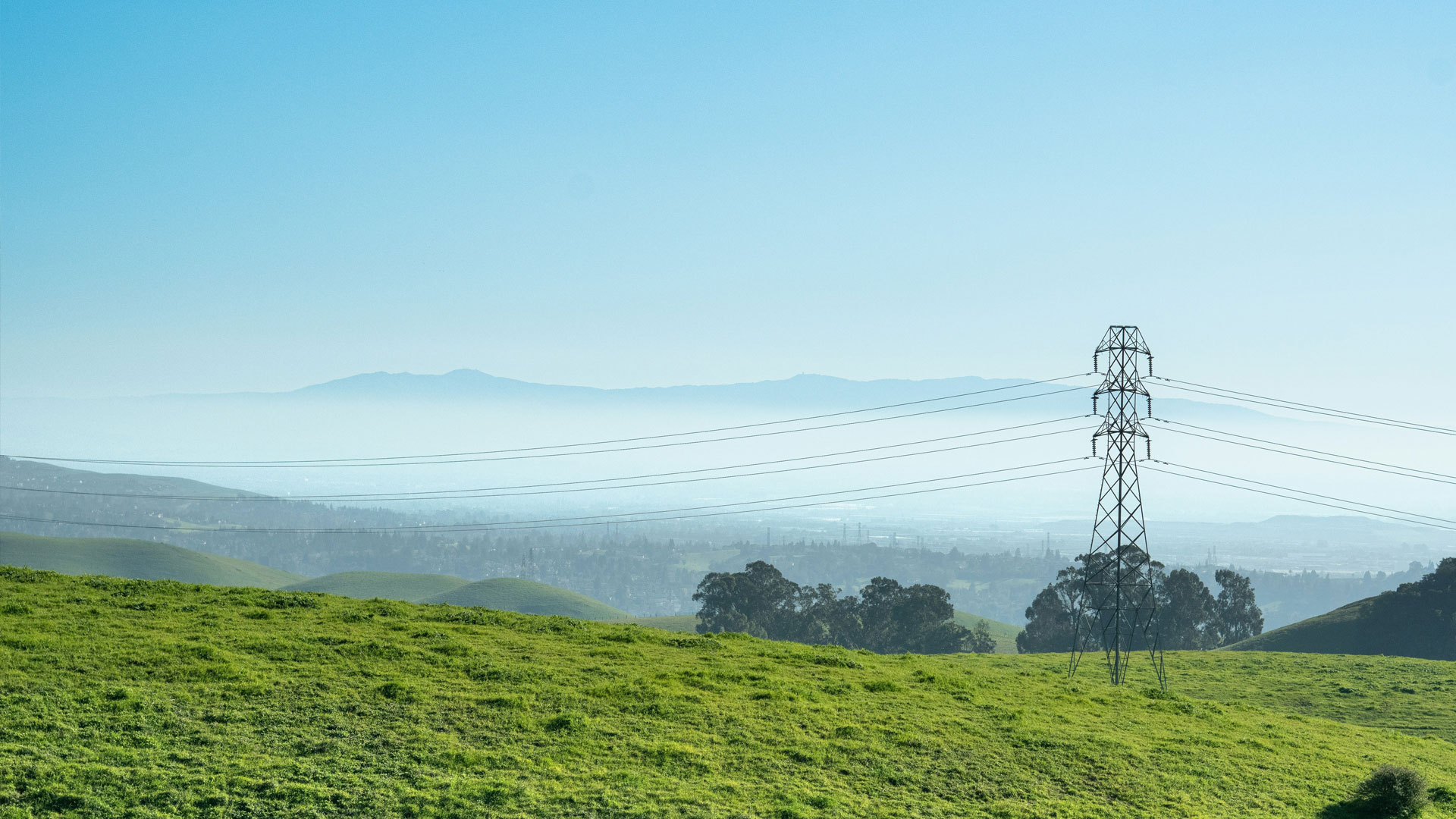 Power transmission lines over green fields with urban area in the distance